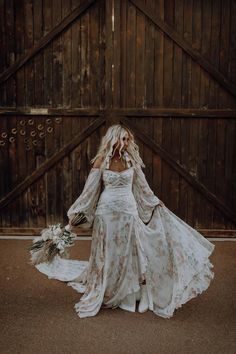 a woman in a white wedding dress holding a bouquet and standing next to a wooden wall