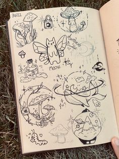 an open book with drawings on it sitting in the grass next to someone's hand