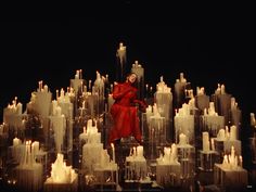 a woman sitting on top of a giant pile of candles in front of a black background