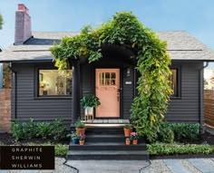 a small gray house with a pink door and some plants on the front porch,