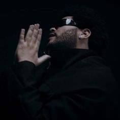 a man wearing sunglasses and holding his hands up in the air while standing against a black background