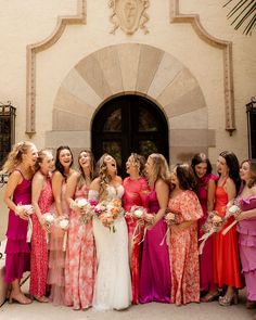 a group of women standing next to each other in front of a building holding bouquets