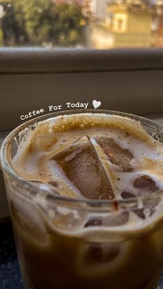 an iced drink in a glass on a table next to a window with the words coffee for today written above it