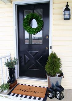 a black front door with a welcome mat and two potted plants on the porch