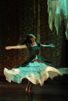 a woman in a green dress is dancing on the stage with her arms spread out