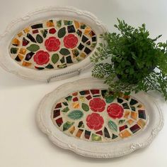 two decorative plates with flowers on them next to a potted plant