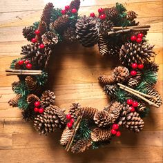 a wreath made out of pine cones and red berries on a wooden floor with cinnamon sticks