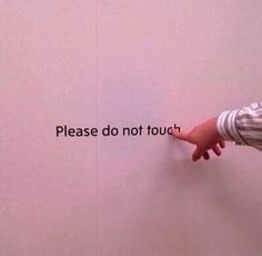 a person pointing at a sign that says please don't touch on the wall