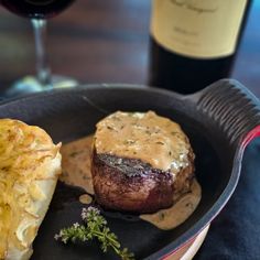 steak and potatoes in a cast iron skillet next to a bottle of wine