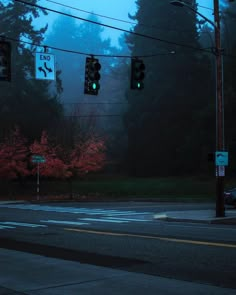 the traffic lights are green at an intersection on a foggy night with trees in the background