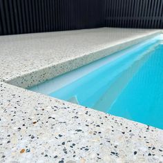 an empty swimming pool with blue water and pebbles on the ground in front of it