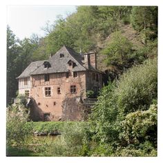 an old brick building sitting on top of a lush green hillside next to a forest