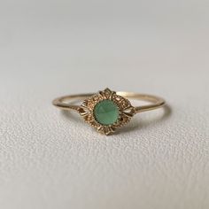 a gold ring with a green stone in the center on a white surface, close up