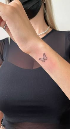 a woman with a small butterfly tattoo on her left arm, wearing a black top