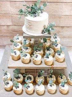 a wedding cake and cupcakes with greenery on the top are sitting on a table