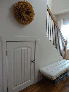 a white bench sitting in front of a door next to a stair case with a wreath on the wall