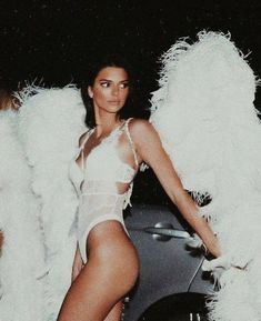 a woman in a white bodysuit standing next to a car with angel wings on it