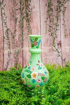 a green vase with flowers painted on it sitting in the grass