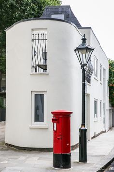 a red mail box sitting next to a lamp post in front of a white building