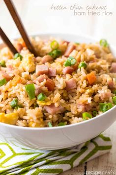 a bowl filled with rice, ham and green onions next to wooden chopsticks