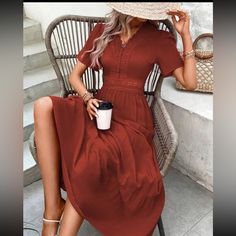 a woman in a red dress and hat sitting on a chair holding a coffee cup