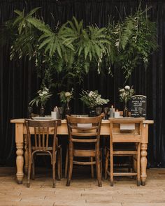 a wooden table topped with lots of green plants next to a black curtained wall