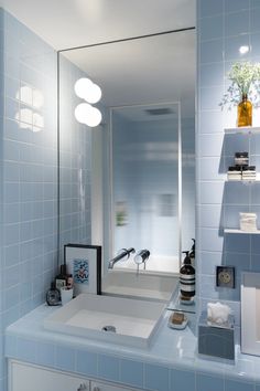 a bathroom with blue tiles and a mirror on the wall above the sink is a vase filled with flowers