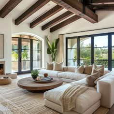 a living room with white couches and wooden beams in the ceiling, along with large windows