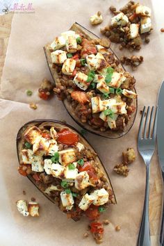 two stuffed eggplant halves are sitting on a piece of parchment paper next to a fork and knife