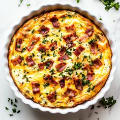 a quiche with bacon and cheese in a white pie dish on a marble surface