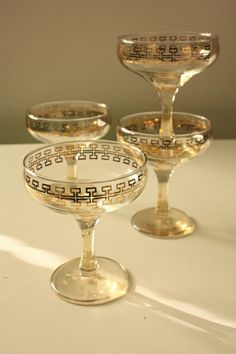 three glass goblets sitting on top of a white table next to each other