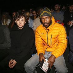 two young men sitting next to each other in front of an audience at a fashion show