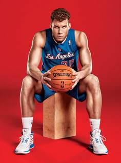 a man sitting on top of a wooden block holding a basketball