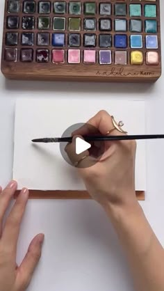 a woman is drawing with watercolors on a piece of paper and holding a pencil