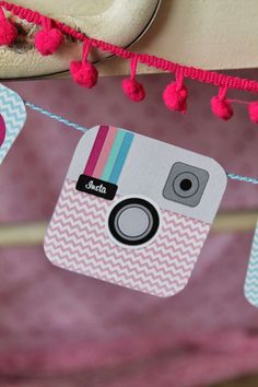 a camera hanging from a string with pink pom - poms