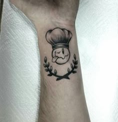 a small tattoo on the wrist of a person wearing a chef's hat and laurels