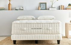 a bed with two pillows on top of it in front of a white wall and bookshelf