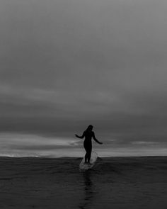 a woman is standing on a surfboard in the ocean at sunset or dawn with her arms outstretched