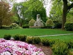 a garden with flowers and a statue in the middle, surrounded by green lawning