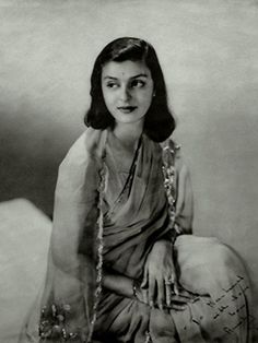 an old black and white photo of a woman in sari sitting on a bed