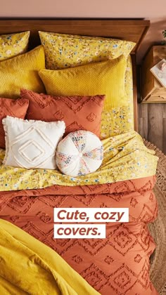 a bed with yellow and orange comforters, pillows and blankets on top of it