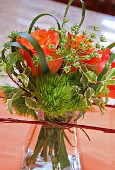 an arrangement of flowers in a vase on a table with red and green foliages