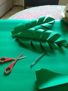 scissors and green paper on a table with some cut up leaves next to it,