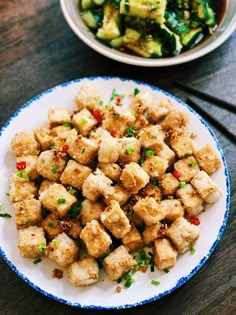 a white plate topped with tofu next to a bowl of broccoli