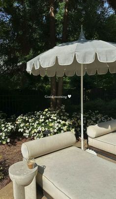 an umbrella sitting on top of a wooden table next to white chairs and flowers in the background