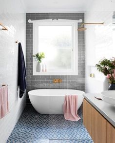 a white bath tub sitting under a bathroom window next to a sink and counter top