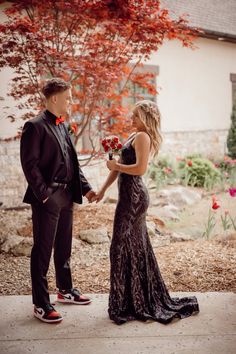 a man and woman standing next to each other in front of a tree with red flowers