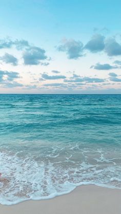 a woman standing on top of a sandy beach next to the ocean under a cloudy blue sky