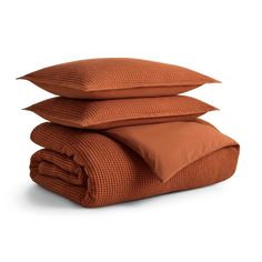 three pillows stacked on top of each other in front of a white background with an orange blanket