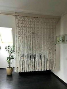 a room with a potted plant on the floor next to a white curtain and shelves